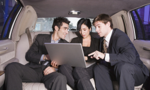 Three businesspeople looking at laptop in limousine
